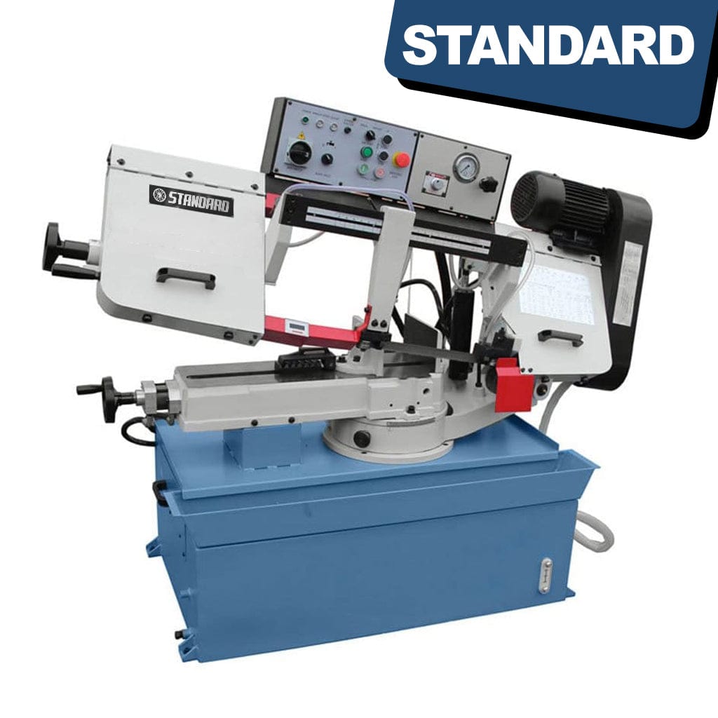 An image of the STANDARD BM-230 Manual Swing Head Bandsaw. The bandsaw is a stationary machine with a large base and a vertical metal frame. The cutting blade is visible, suspended vertically from the top, with an adjustable head that can swing to different angles for cutting. The machine has control knobs and handles for manual operation. Safety guards and guides are in place around the blade area.