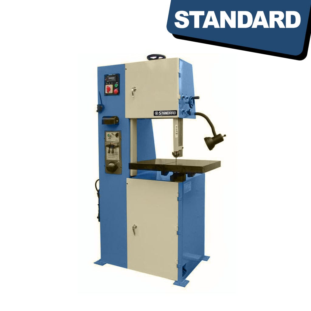 STANDARD BV-320x590 Vertical Bandsaw. A vertical metal-cutting bandsaw machine with a sturdy frame, cutting blade, and control panel. The machine stands against a workshop background with safety features and adjustable components visible.